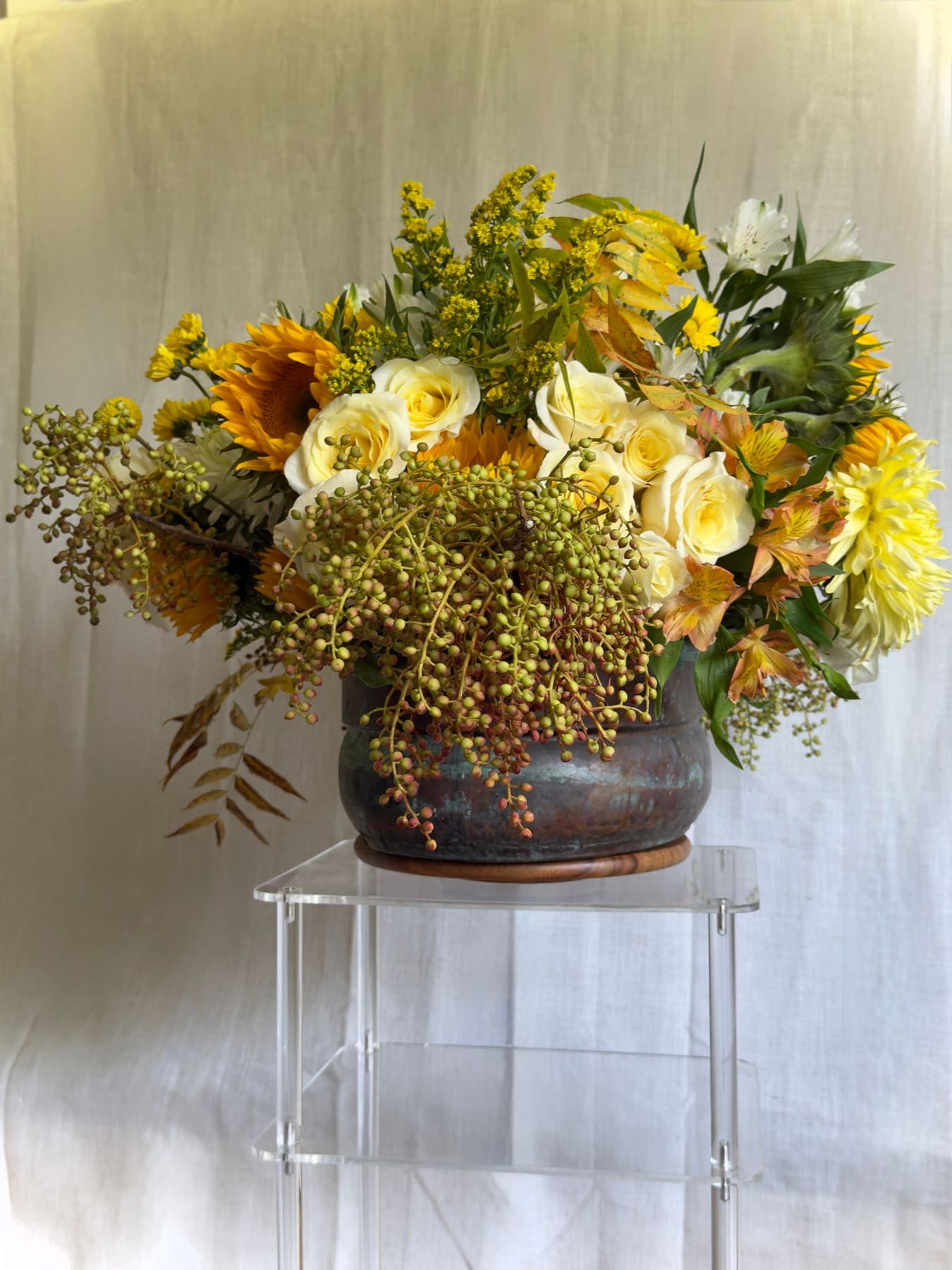 Sunflowers, roses, and trailing berries in an aged bronze urn
