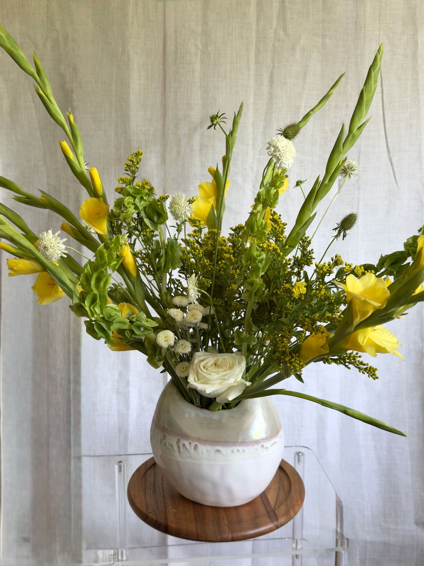 Tall yellow gladiolus and goldenrod in a round white vase