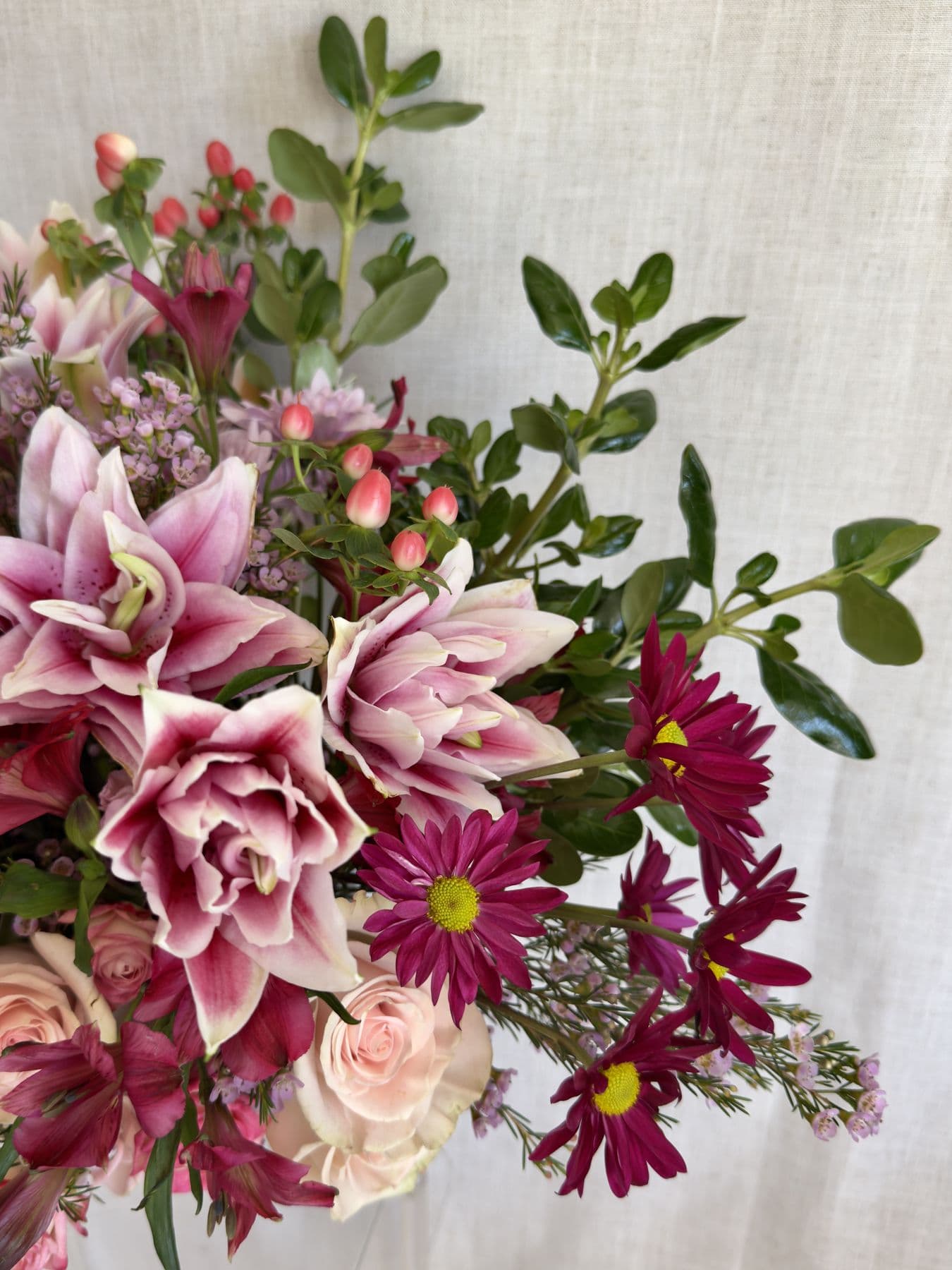 Pink lilies, blush roses, magenta daisies, and coral berries on linen