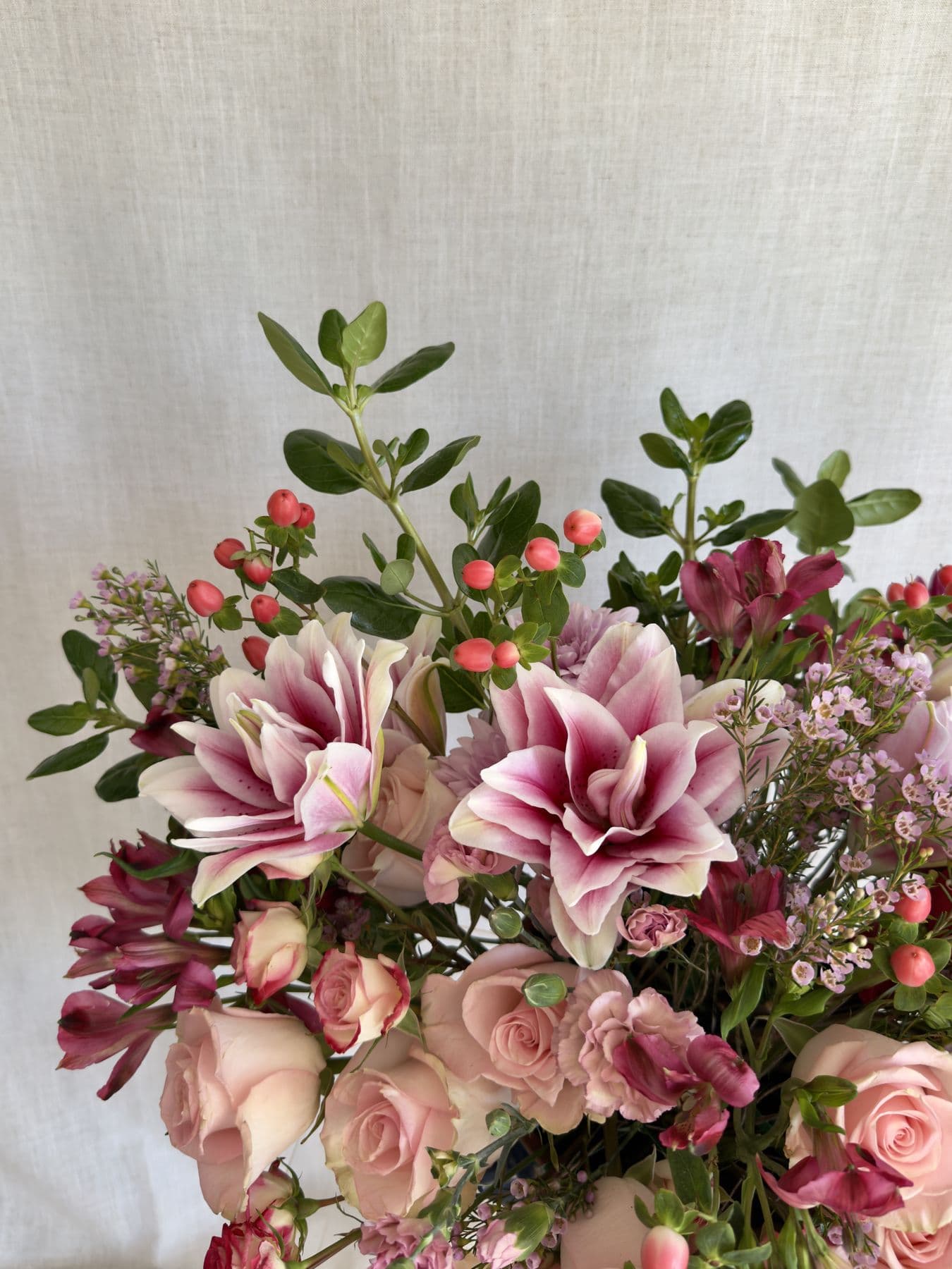 Pink lilies, blush roses, and coral hypericum berries on linen