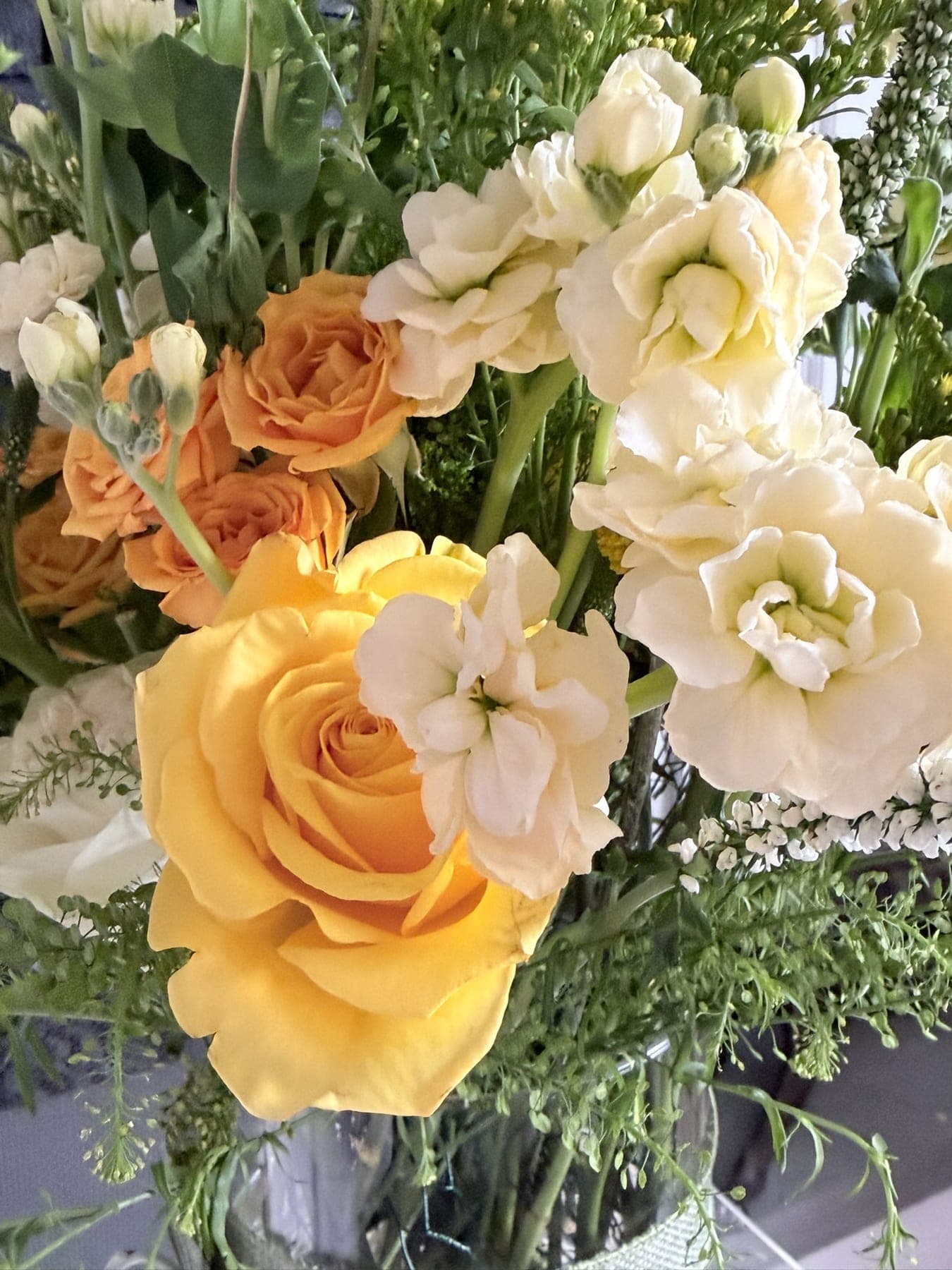 Close view of yellow roses, orange spray roses, and cream stock